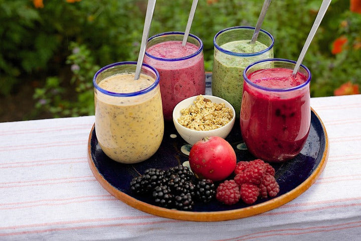 Auf einem Tablett stehen vier verschiedene Smoothie´s. Davor liegen einige Früchte